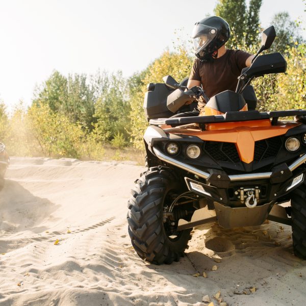 Two atv riders in helmets ride in a circle on sand